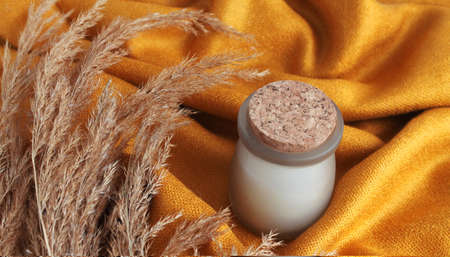 white candle in a jar with branches of dry pampas grass on the background of gold cloth. Autumn themeの写真素材