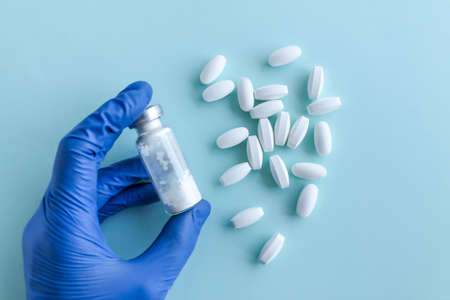 A hand in a blue medical glove holds a handful of white pills, next to it are a bottle of white powder on a light blue background. Top view, flatlayの写真素材
