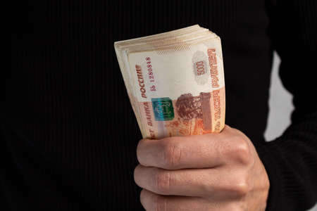 Close-up of mens hands holding a wad of Russian money with five-thousand-dollar bills. High quality...