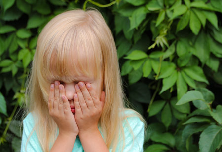 A little blonde girl cries, covers her face with her hands, feels emotions of sadness.の写真素材