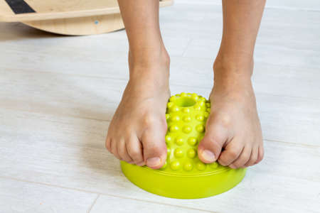 The child performs exercises on the balancer from the valgus of the foot. The childs legs are close-up. Physical therapy classes for children. Foot massageの写真素材