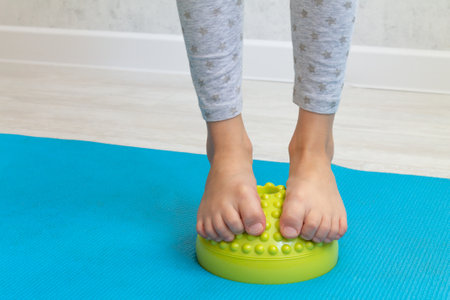 The child performs exercises on the green balancer from the valgus of the foot. The childs legs are close-up. Physical therapy classes for children. Foot massageの写真素材