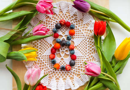 A composition of tulip flowers and the number 8 for the holiday of the eighth of March. The number 8 is laid out from miniature fruits made of polymer clay on a lace napkin. international womens dayの写真素材