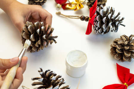Handmade toy for the Christmas tree from pine cones. Childrens creativity. Hands close-up paint the cone with white paint.の写真素材