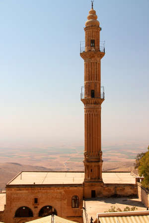 View of the Sehidiye Mosque with its tall minaret and the Mesopotamian Valley in light haze in the background in the city of Mardin in the Southeast Anatolia region of Turkeyの写真素材