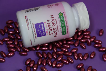 Kyiv, Ukraine - April 30, 2023: Bottle and burgundy capsules of vitamins for hair, skin and nails with Biotin 5000 mcg manufactured by Nature's Bounty on a purple backgroundのeditorial素材