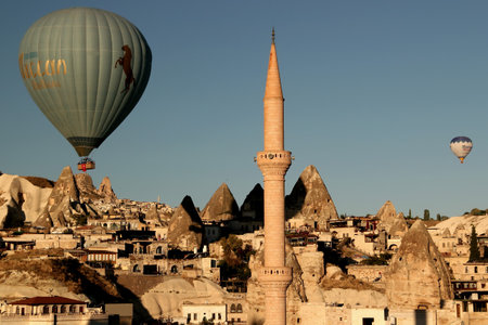 Goreme, Cappadocia, Turkey - August 30, 2020:Panoramic view of Goreme with cone-shaped cave houses and a mosque with a minaret in the center of the photo and two balloonsのeditorial素材
