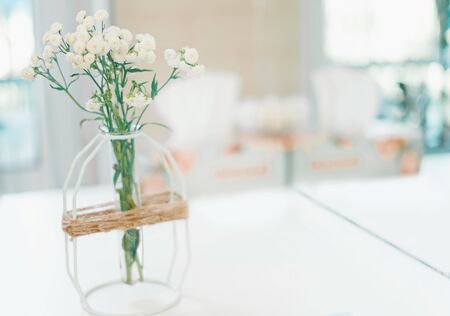 a small vase of flowers stands on a white table against a bright window