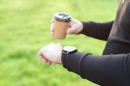 the man looks at the mockup of the hand watch. in the hand of a craft cup on a green background