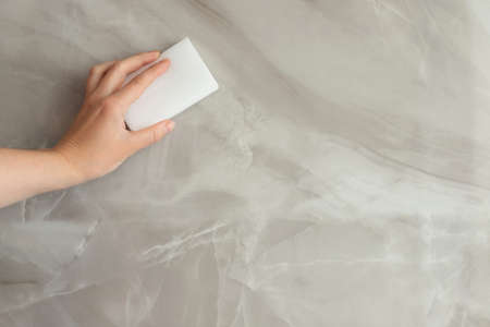 a woman wipes a gray tile with a melanin sponge. close upの写真素材
