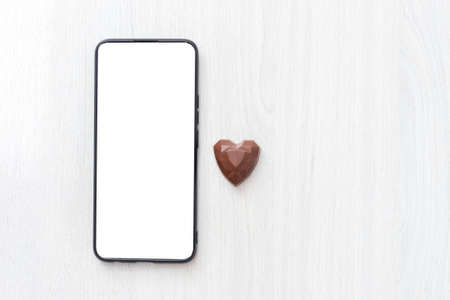 mock ap smartphone and chocolate heart on a light wood background