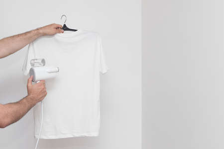 Steam the T-shirt with a portable steamer on a white background. copyspace
