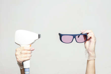 accessories for laser hair removal in hands. diode laser and safety glasses on white backgroundの写真素材