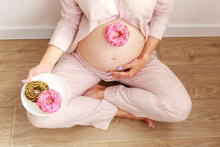 Pregnancy and unhealthy eating concept: pregnant woman with tasty donuts close-upの写真素材