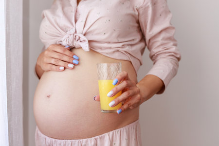 Pregnancy, people and rest concept - happy pregnant woman drinking or holding orange juice at homeの写真素材