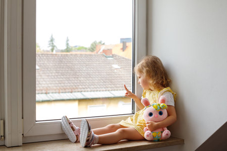a 4-year-old girl sits on the window and points out the windowの写真素材