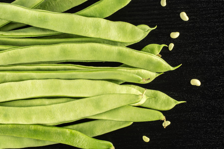 Flat green beans with seeds top view isolated on black wood background