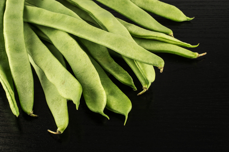 Flat green beans isolated on black wood background top view