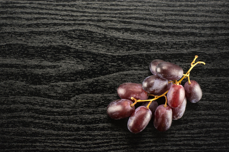 Red globe grapes one cluster table top isolated on black wood background shiny deep pink berriesの写真素材