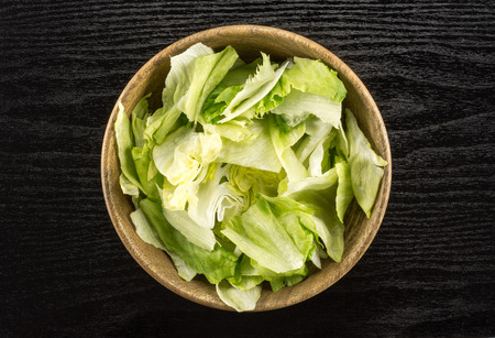 Iceberg lettuce table top fresh torn salad leaves in a wooden bowl isolated on black wood backgroundの写真素材