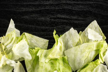 Iceberg lettuce fresh torn salad leaves stack table top isolated on black wooden backgroundの写真素材