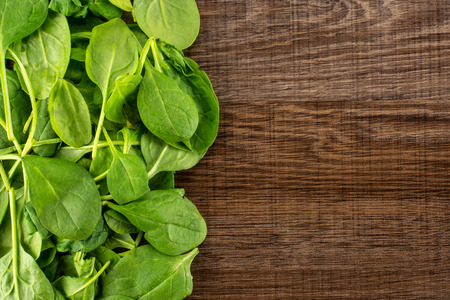 Fresh baby spinach leaves top view on brown wood background left corner
