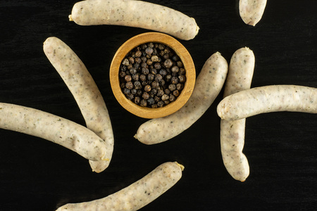Lot of whole bavarian white sausage and black pepper in a wooden bowl flatlay on black wood