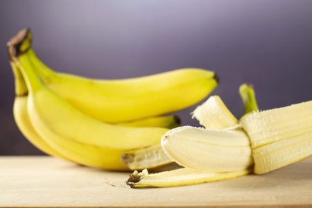 Lot of whole fresh yellow banana one cluster and opened like a plane with grey gradient behindの写真素材