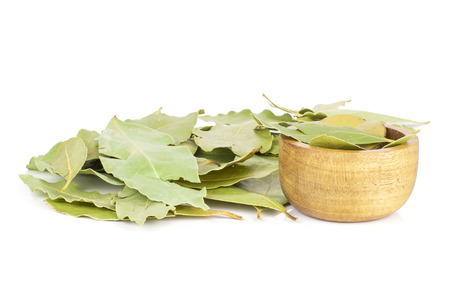 Lot of whole dry olive green bay laurel leaves with wooden bowl isolated on white background