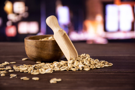 Lot of whole flat raw rolled oats scoop in front with wooden bowl with restaurant in background