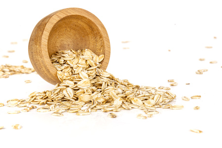 Lot of whole pouring flat raw rolled oats with wooden bowl isolated on white backgroundの写真素材