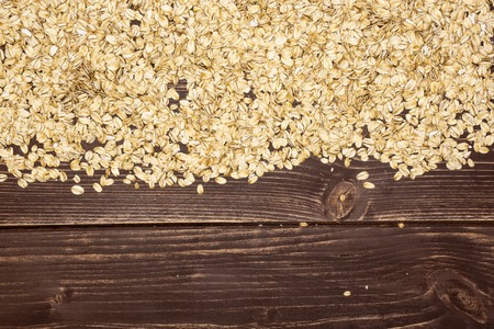 Lot of whole flat raw rolled oats above flatlay on brown woodの写真素材