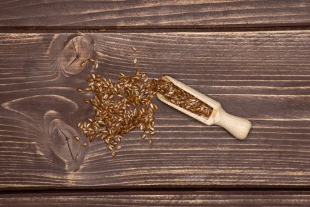 Lot of whole fresh brown flaxseeds with wooden scoop flatlay on brown woodの写真素材