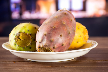 Group of three whole fresh bright prickly pear opuntia on white porcelain plate with restaurant in backgroundの写真素材