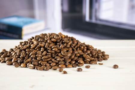 Lot of whole dark brown coffee beans sweet arabica variety with books near the window in backgroundの写真素材