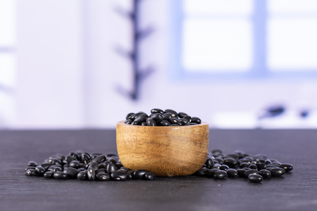 Lot of whole raw black turtle beans with wooden bowl with blue window in background