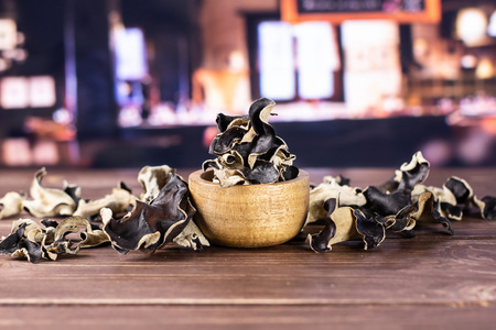 Lot of slices of edible dry black mushroom jew ear variety with wooden bowl with restaurant in backgroundの写真素材