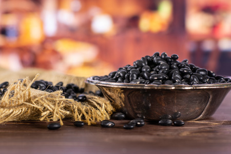 Lot of whole raw black turtle beans in old iron bowl with rustic wood kitchen in backgroundの写真素材