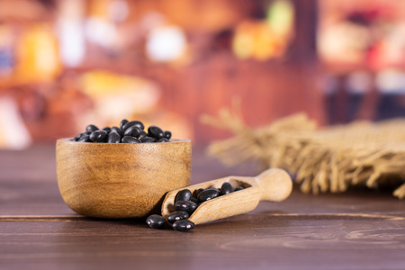 Lot of whole raw black turtle beans in a scoop with wooden bowl with rustic wood kitchen in backgroundの写真素材