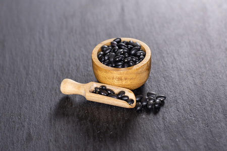 Lot of whole raw black turtle beans in a scoop with wooden bowl on grey stone