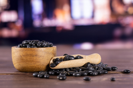 Lot of whole raw black turtle beans in a scoop with wooden bowl with restaurant in backgroundの写真素材