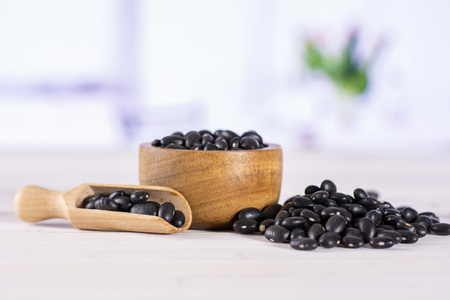Lot of whole raw black turtle beans in a light scoop with wooden bowl with red flowers on white in backgroundの写真素材