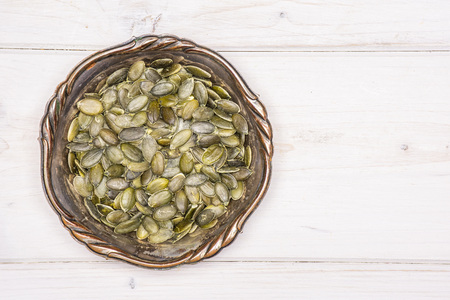Lot of whole hulled pumpkin seeds in old iron bowl flatlay on white woodの写真素材