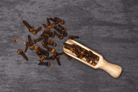 Lot of whole small dried cloves spice with wooden scoop flatlay on grey stone