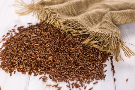 Lot of whole raw red rice on jute cloth on white woodの写真素材