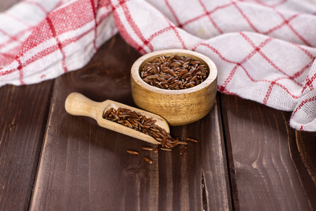 Lot of whole raw red rice tea towel and a scoop with wooden bowl on brown wood