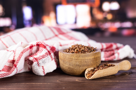 Lot of whole raw red rice tea towel with wooden bowl with restaurant in backgroundの写真素材