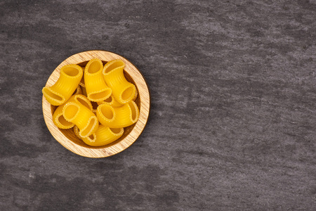 Lot of whole raw pasta pipe rigate variety with wooden bowl flatlay on grey stone