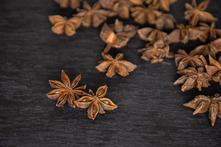 Group of two whole dry brown star anise fruit in a focus and a stack on grey stoneの写真素材