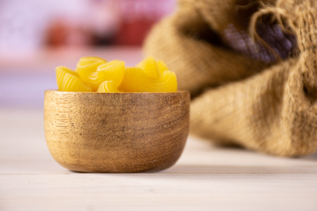 Lot of whole yellow raw pasta pipe rigate variety with wooden bowl in white kitchen